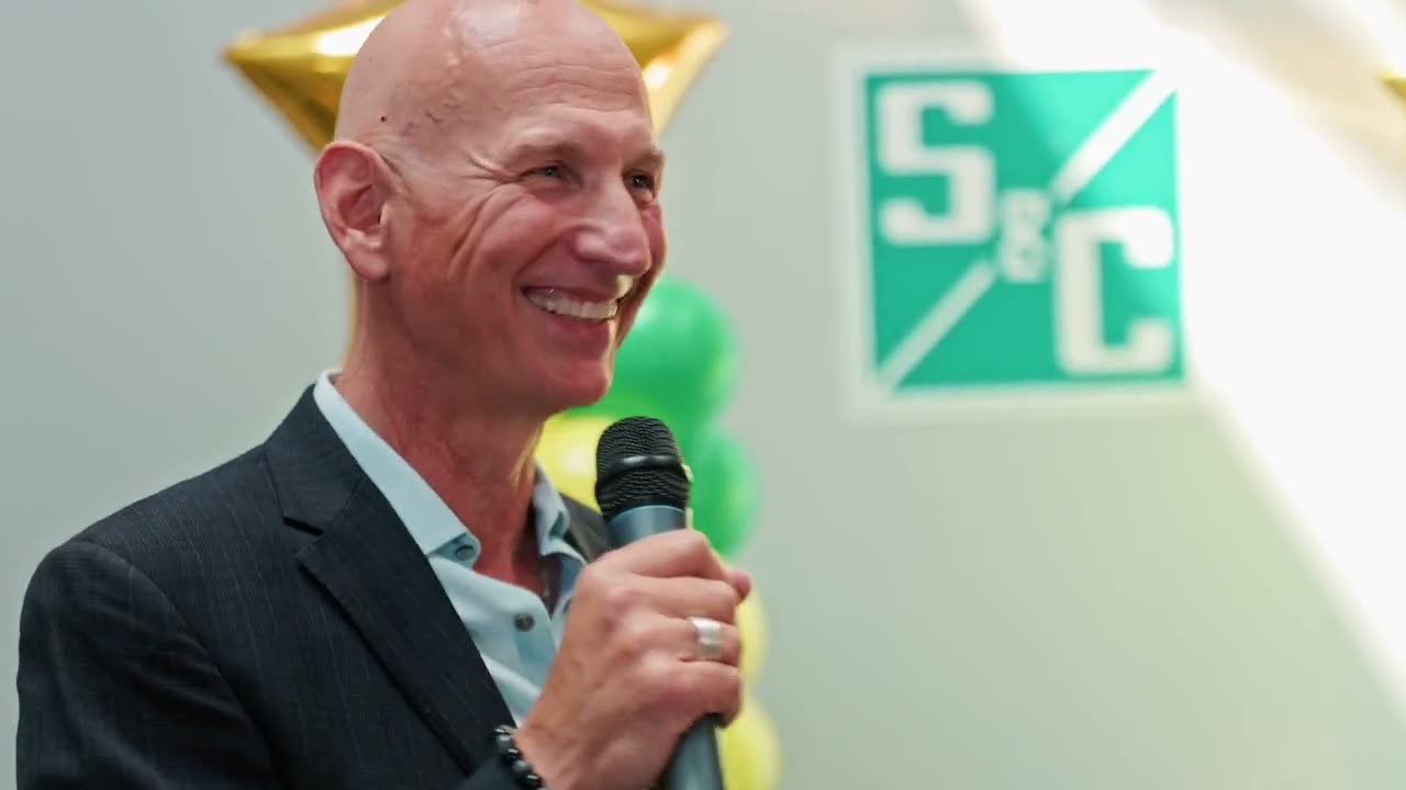 An S and C Electric Canada leader speaking with a microphone at a staff celebration