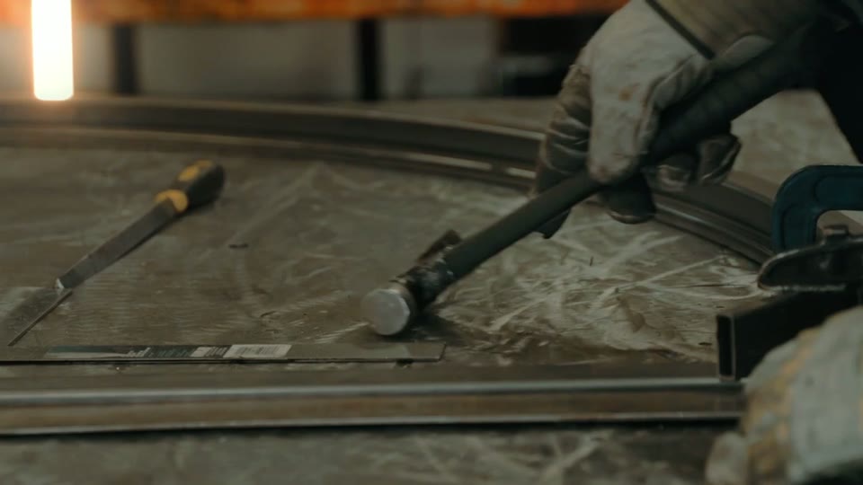 A gloved hand shaping a metal frame on a workbench, from the Conform Glass film